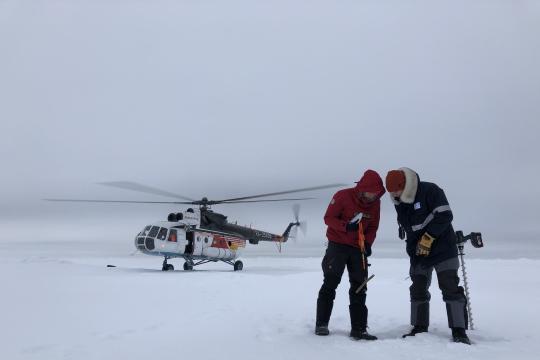 Two scientists on ice, helicopter in background