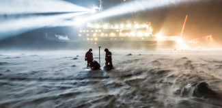 Two researchers work on the ice in front of the German research icebreaker Polarstern. Photo: AWI scientists in blowing snow, dark