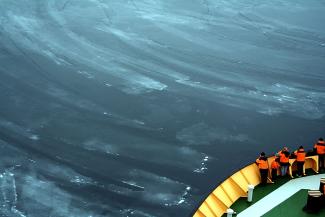 A 2005 photograph captures the essence of nilas sea ice in Baffin Bay. Photo: Brocken Inaglory/Wikimedia Commons people looking over edge of ship into nilas sea ice