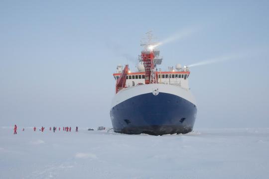 small people in a line on the ice, beside icebreaker